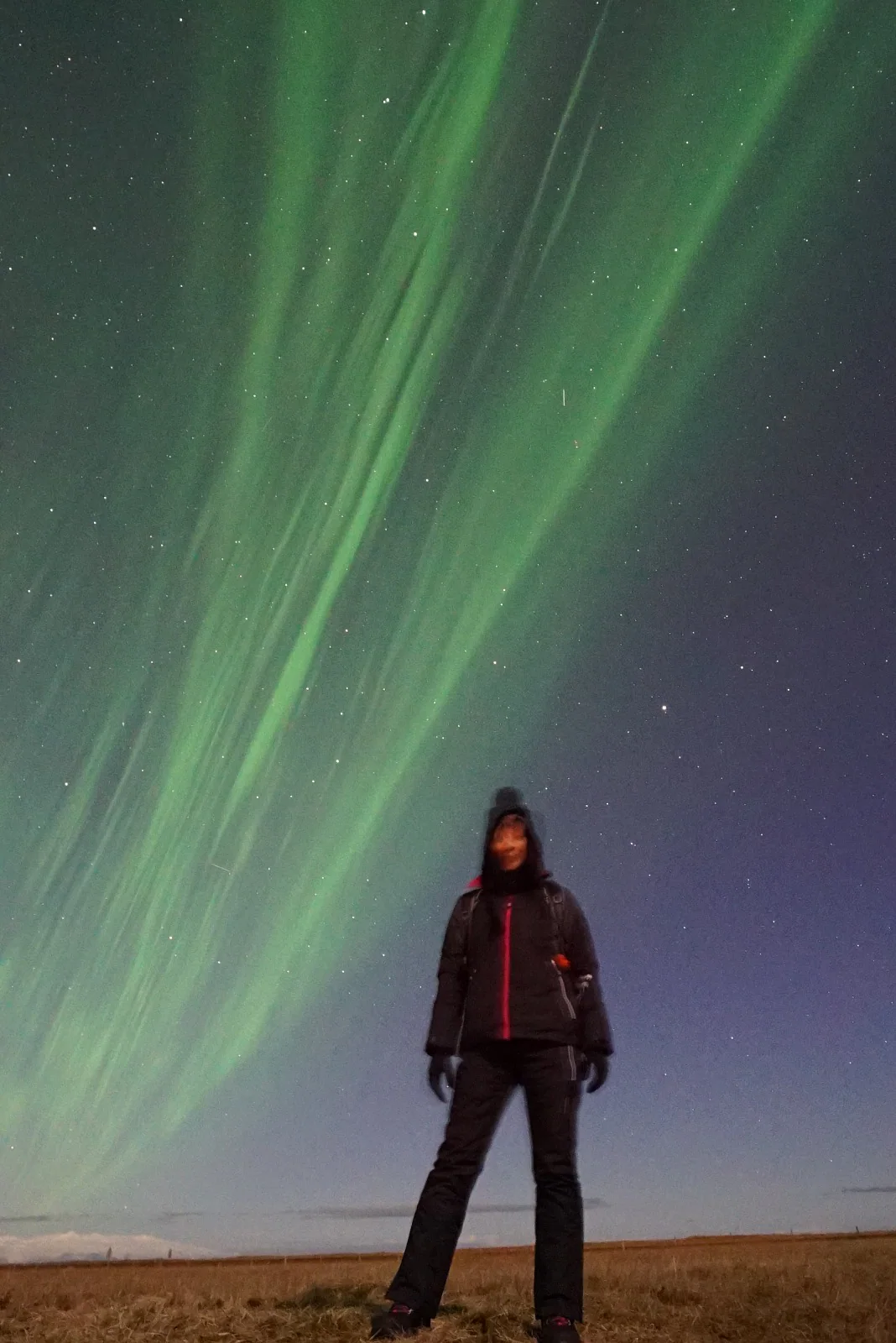 Una figura in piedi nella notte sotto un'aurora boreale verde