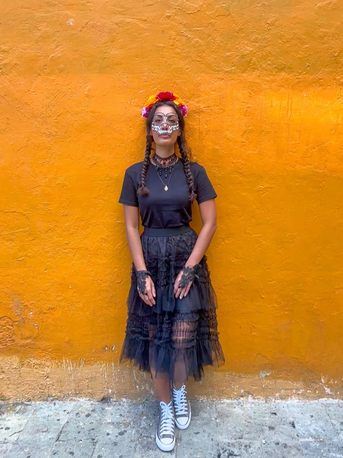 Samira con trecce e fiori tra i capelli davanti a un muro giallo