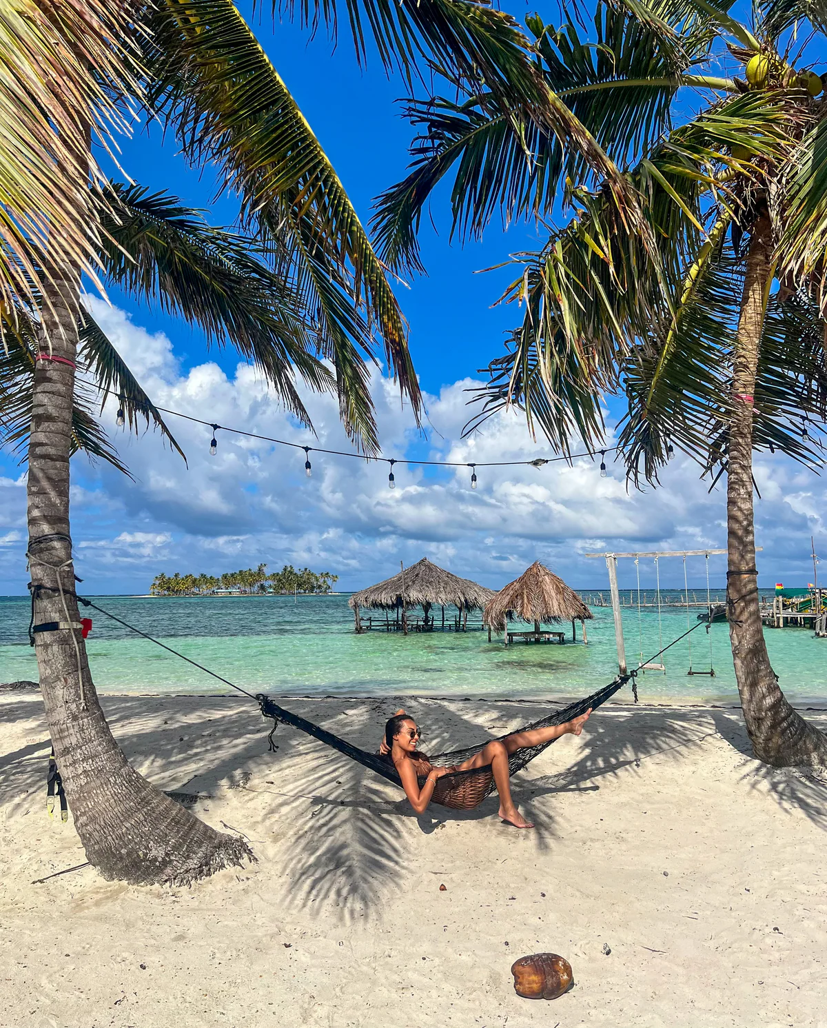 Samira in a hammock slung between palms, on the beach