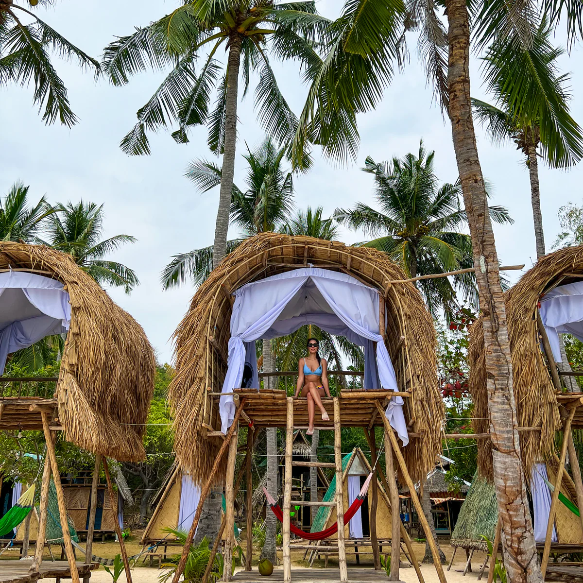 Thatched huts among the palms on a beach, with Samira sitting in the middle one