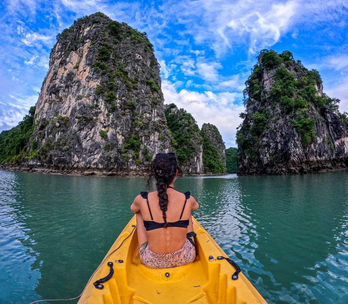 Samira from behind on a yellow kayak, between two karst rock towers