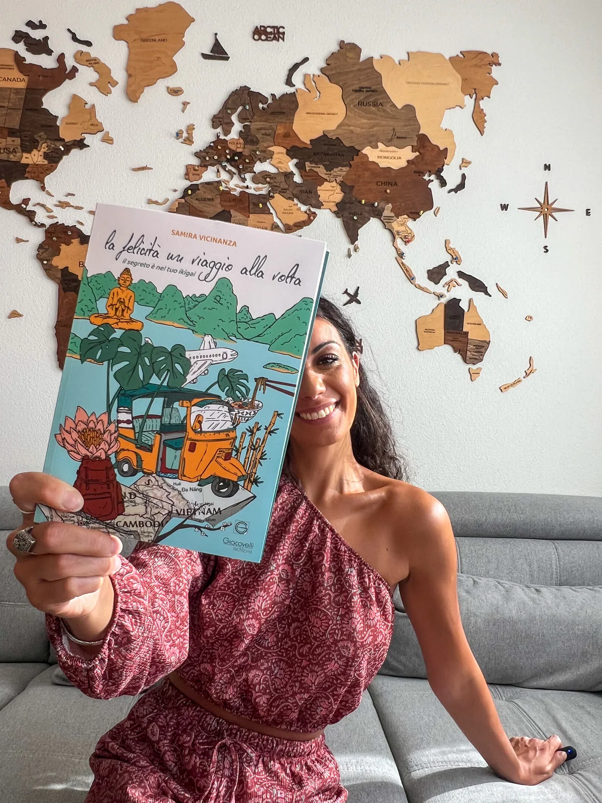 Samira mostra il suo libro davanti a una mappa del mondo in legno