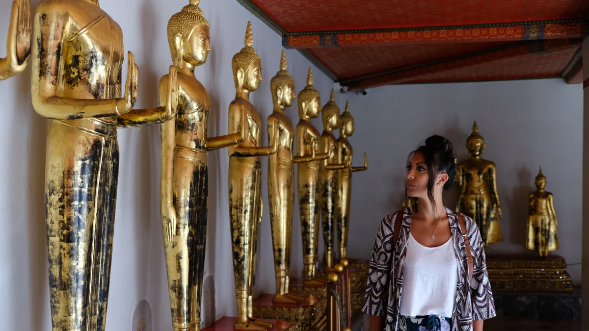 Samira next to a row of golden Buddha statues