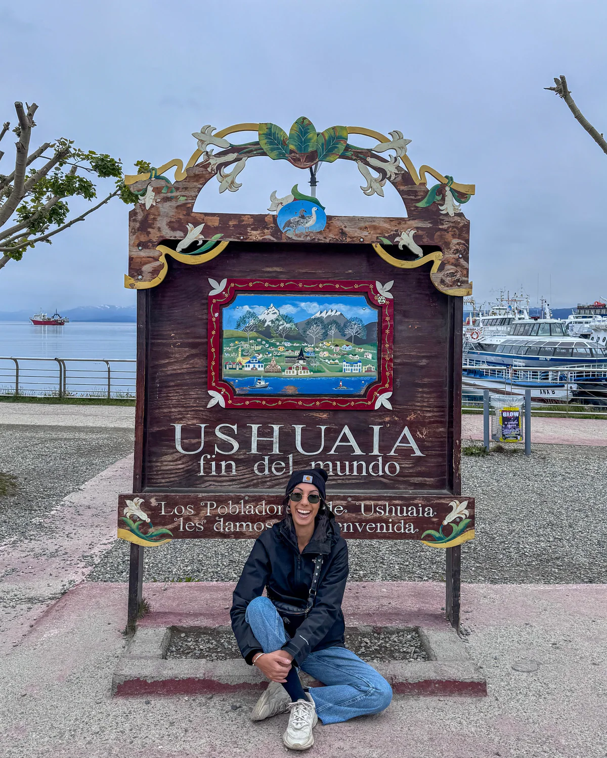 Samira accovacciata sotto il cartello di Ushuaia, fin del mundo