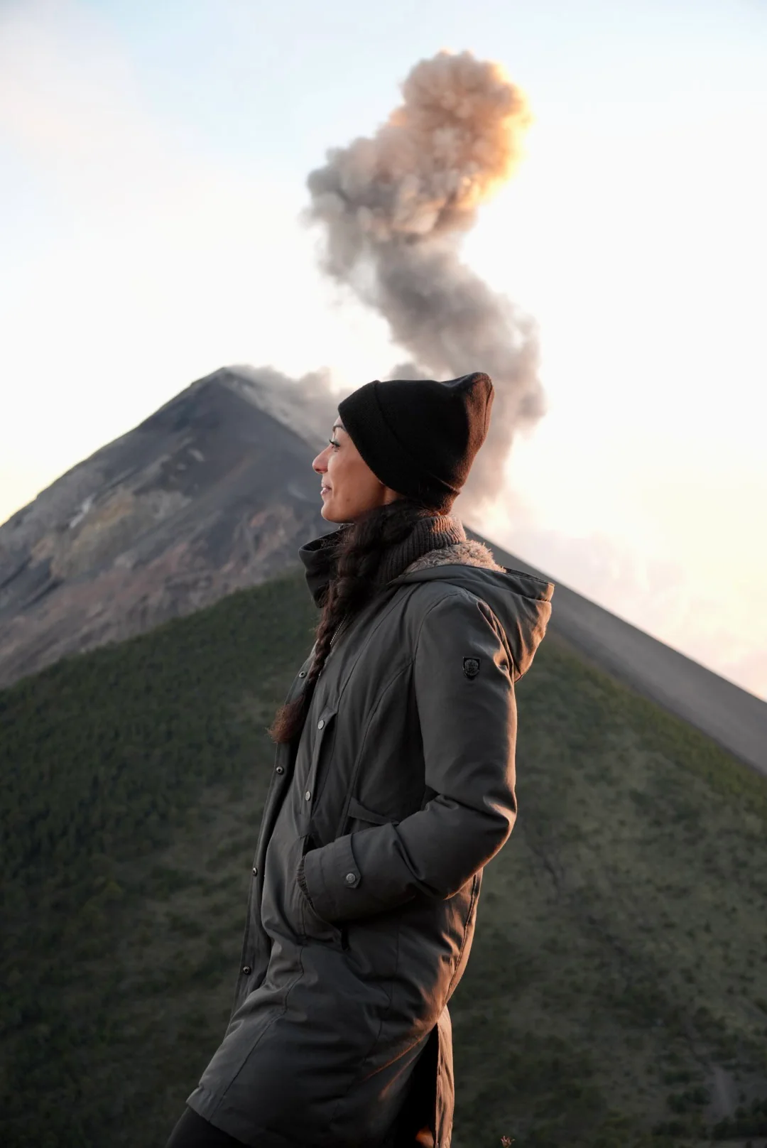 Una persona con il berretto guarda un vulcano che erutta all'alba